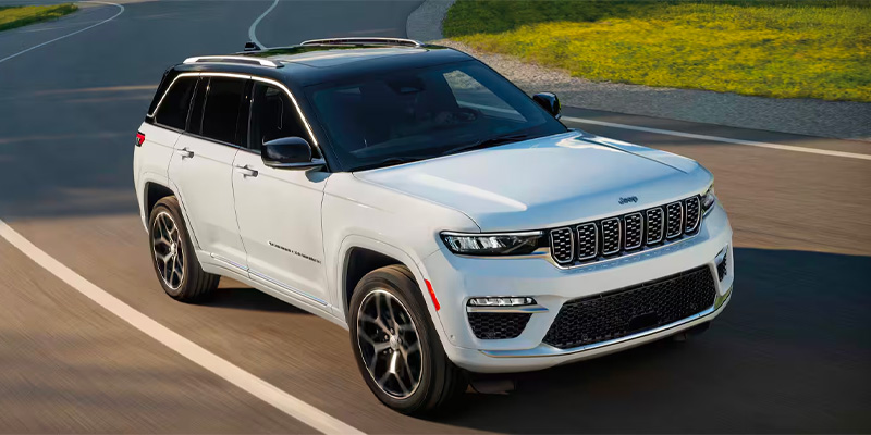 A white 2025 Jeep Grand Cherokee L SUV with a black roof driving on a curved road.
